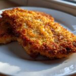 Two pieces of golden brown Air Fryer Crispy Parmesan Pork Schnitzel resting on a white plate.