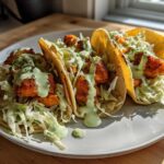 Three Air Fryer Crispy Sweet Potato Tacos filled with slaw and drizzled with green sauce on a white plate.