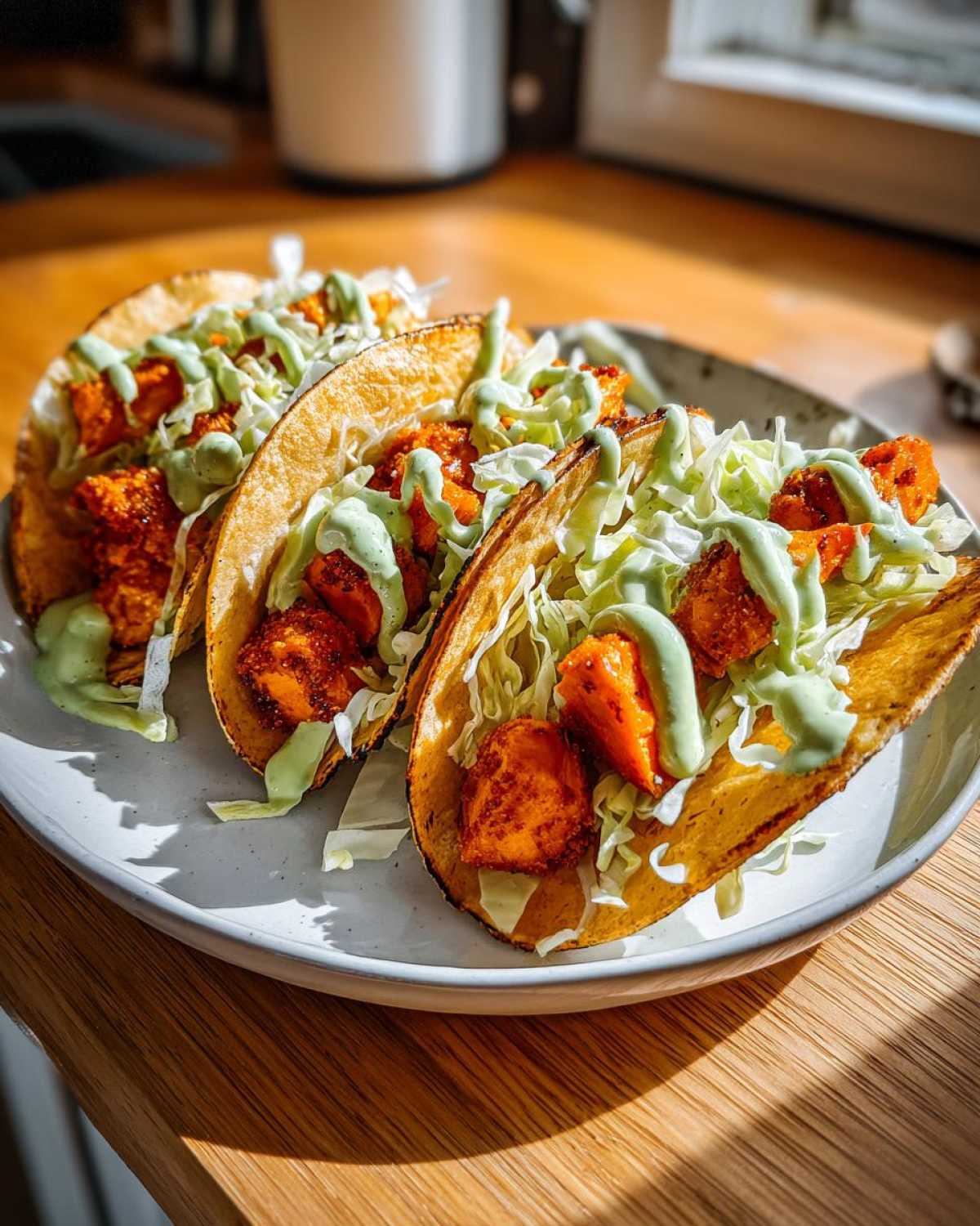 Three crispy tacos filled with seasoned sweet potato chunks, shredded cabbage, and drizzled with green sauce, ready to eat.