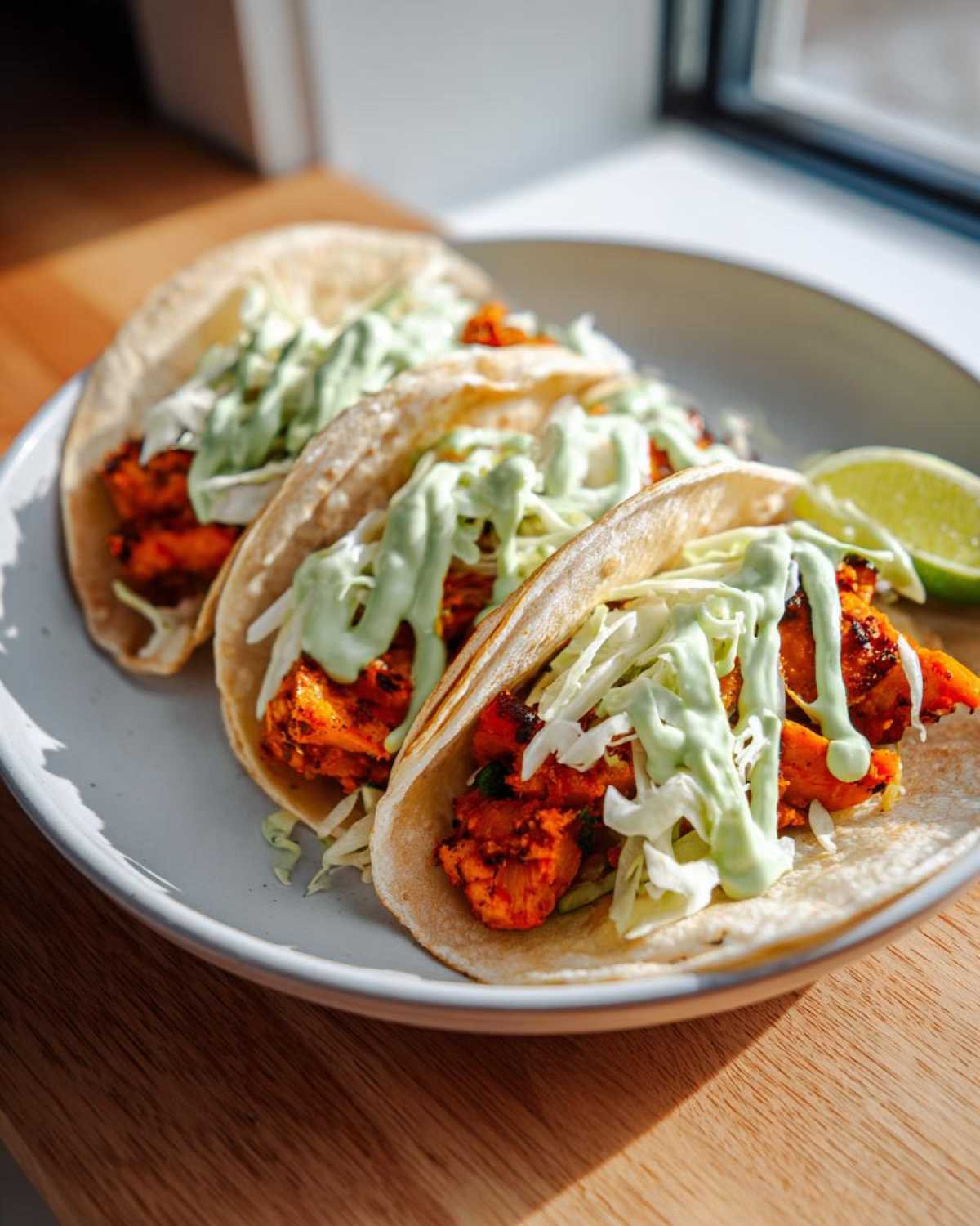 Three soft shell tacos filled with crispy sweet potato, cabbage slaw, and drizzled with green sauce, ready for Air Fryer Crispy Sweet Potato Tacos.