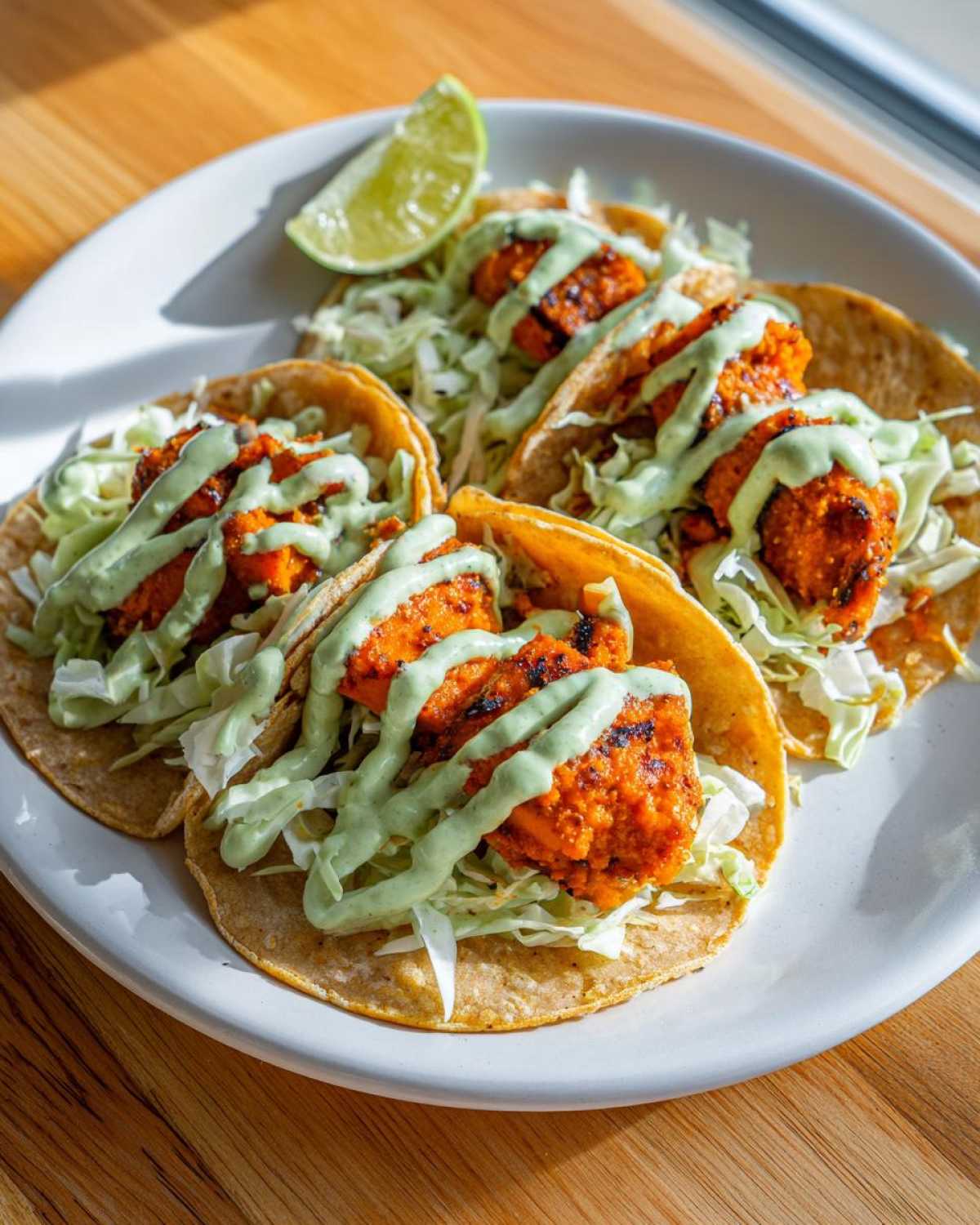 Four Air Fryer Crispy Sweet Potato Tacos topped with shredded cabbage and green sauce, served with a lime wedge.