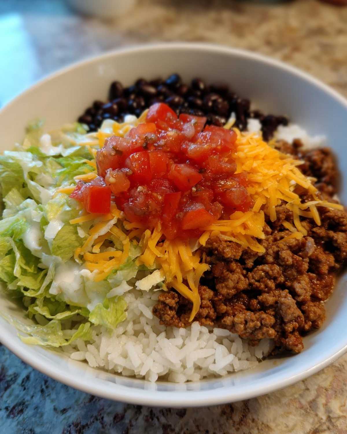 Close-up of a bowl filled with rice, seasoned ground turkey, black beans, shredded cheese, lettuce, and salsa for an Air Fryer Crispy Turkey Taco Bowl.