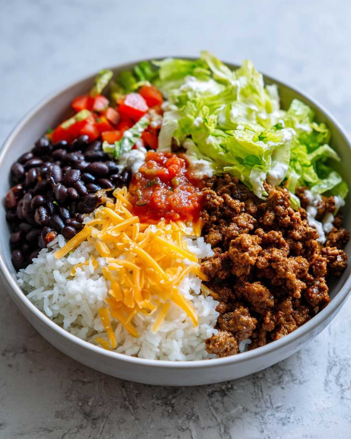 A close-up of a finished Air Fryer Crispy Turkey Taco Bowls, featuring seasoned ground turkey, rice, black beans, cheese, salsa, lettuce, and tomatoes.