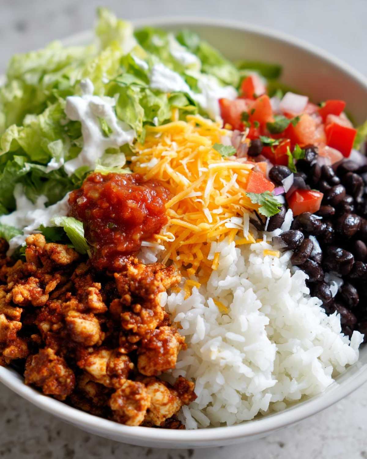 Close-up of an Air Fryer Crispy Turkey Taco Bowls layered with seasoned turkey, rice, black beans, cheese, salsa, lettuce, and tomatoes.