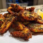 A pile of golden brown, crispy Air Fryer Crispy Zaatar Chicken Wings seasoned with dark spices and herbs, served with a lemon wedge.