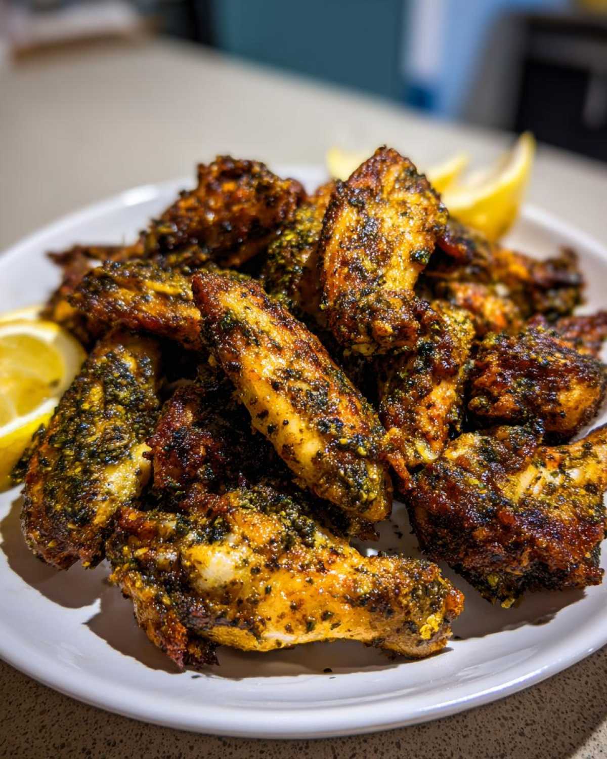 A pile of golden brown, crispy Air Fryer Crispy Zaatar Chicken Wings seasoned heavily with green zaatar spice mix, served with lemon wedges.