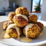 A stack of golden brown Air Fryer Herb Falafel Balls drizzled generously with creamy tahini sauce on a white plate.