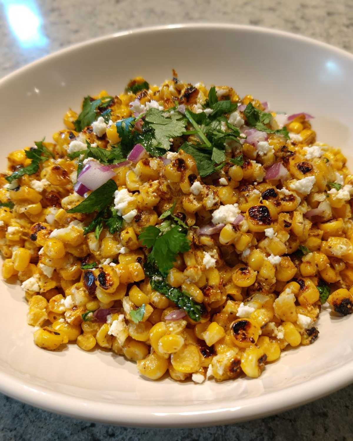 Close-up of charred corn kernels mixed with cotija cheese, red onion, and cilantro, resembling Copycat Mexican Grill Corn Salsa.