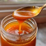A spoonful of thick, amber Copycat Apple Cider Vinaigrette dripping back into a glass jar.