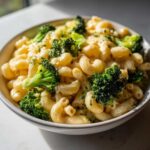 A close-up of a bowl filled with creamy Copycat Café Broccoli Cheddar Mac and bright green broccoli florets.