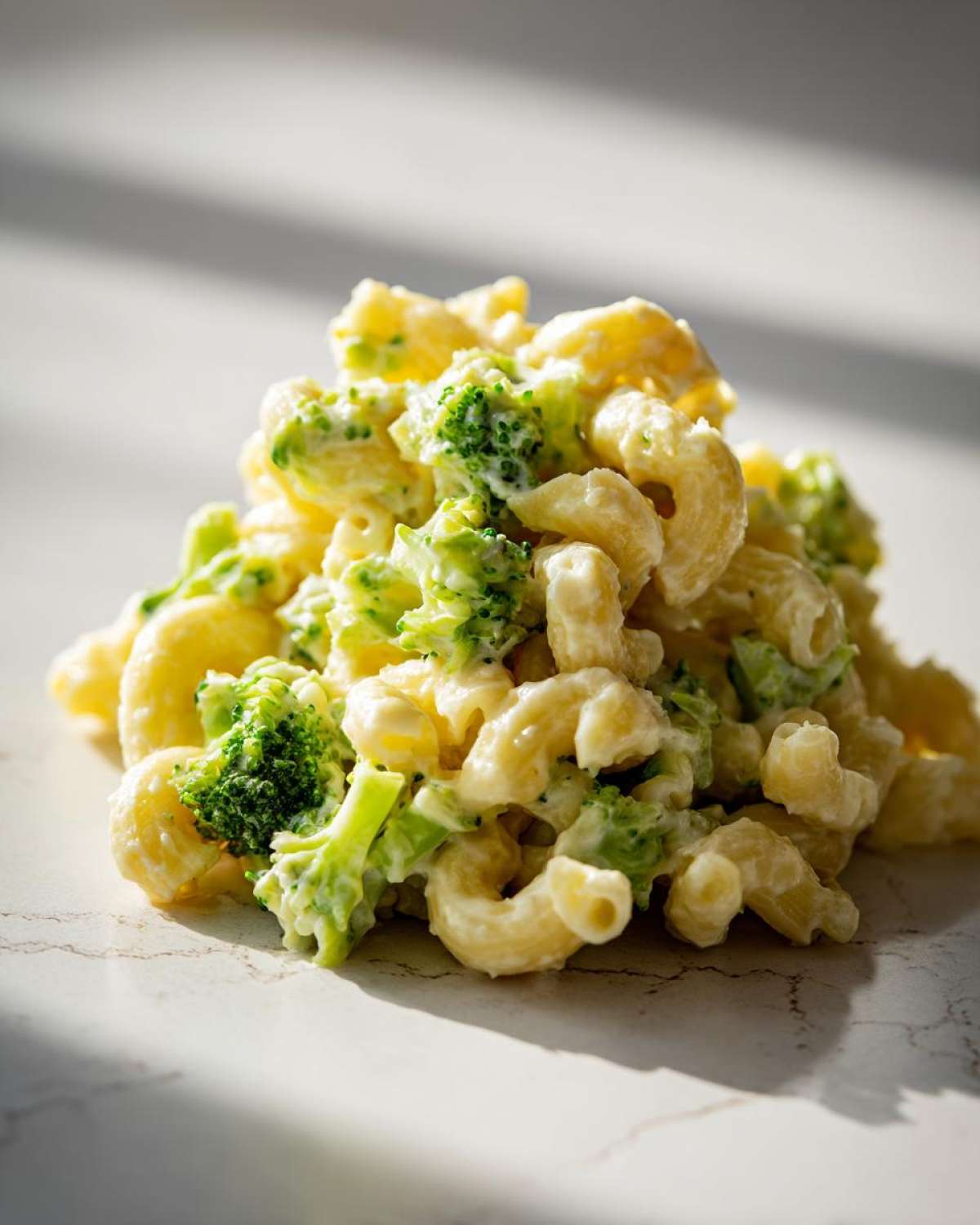 A mound of creamy Copycat Café Broccoli Cheddar Mac featuring elbow macaroni and bright green broccoli florets.