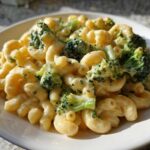 A close-up of creamy Copycat Café Broccoli Cheddar Mac served in a white bowl under natural light.