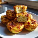A stack of golden-brown Copycat Café-Style Bacon Gruyère Egg Bites piled on a white plate, one cut open showing the fluffy interior.