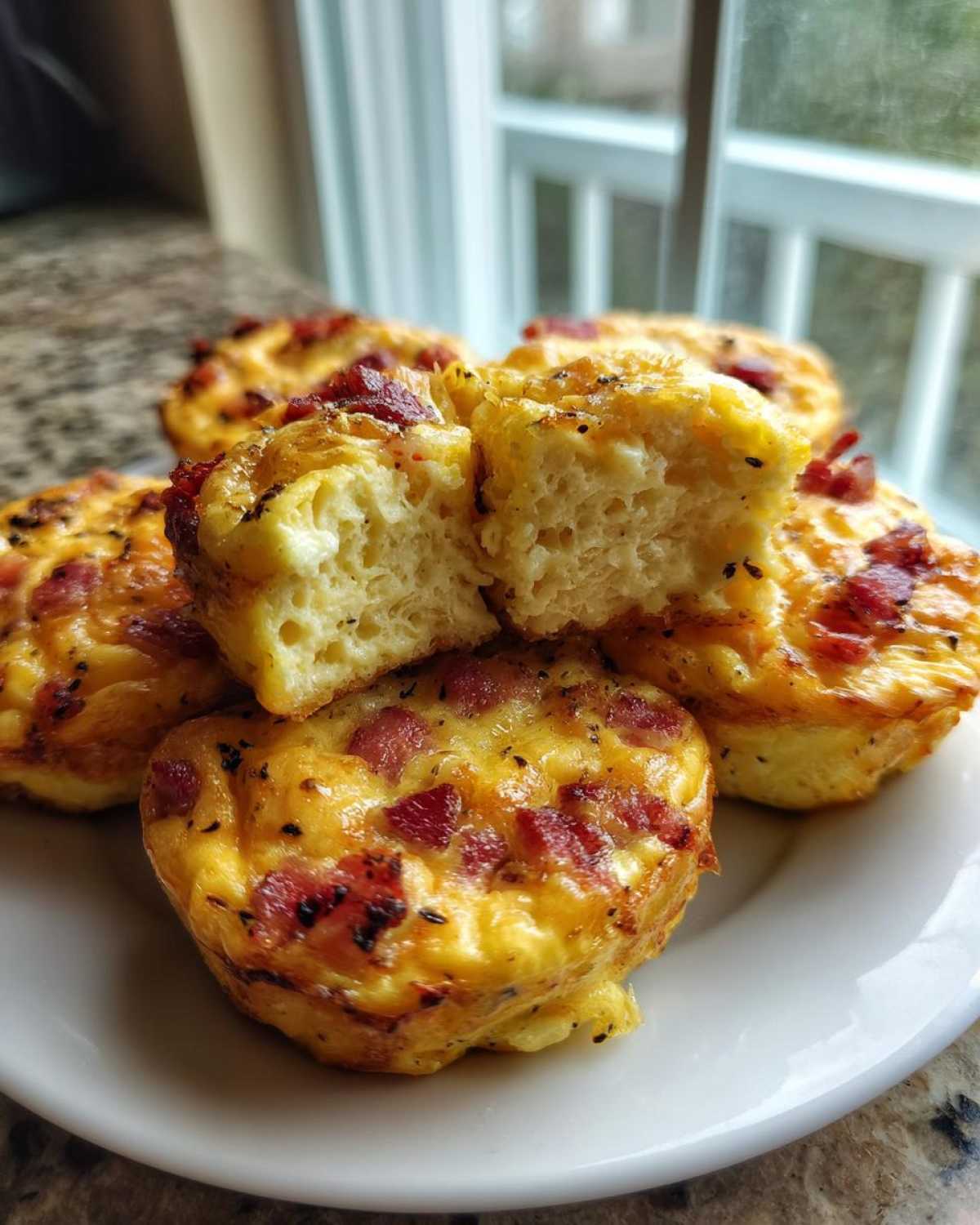 A stack of fluffy Copycat Café-Style Bacon Gruyère Egg Bites on a white plate, one cut open to show the texture.