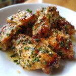 Close-up of crispy chicken wings generously coated in the Copycat Garlic Parmesan Wing Sauce with visible herbs and garlic.