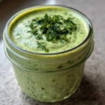 Close-up of creamy, bright green Copycat Green Goddess Ranch Dressing topped with fresh chopped parsley in a glass jar.
