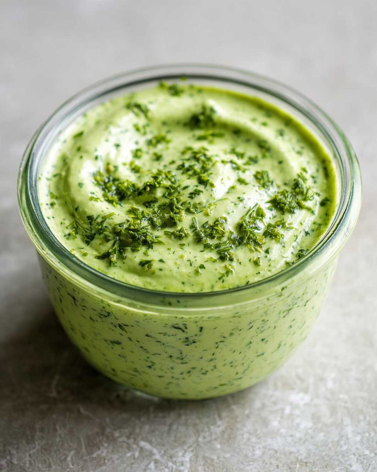 Close-up of thick, vibrant green Copycat Green Goddess Ranch Dressing topped with fresh chopped herbs in a glass jar.