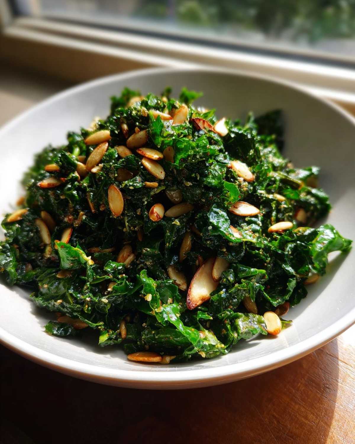 A bowl of vibrant green Copycat Kale Crunch Salad topped generously with toasted sliced almonds and seeds.