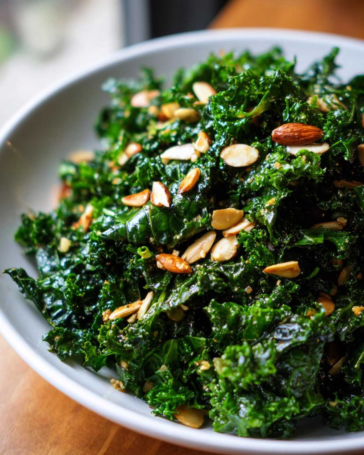 Close-up of vibrant green kale massaged and topped with sliced almonds in a white bowl, representing the Copycat Kale Crunch Salad.