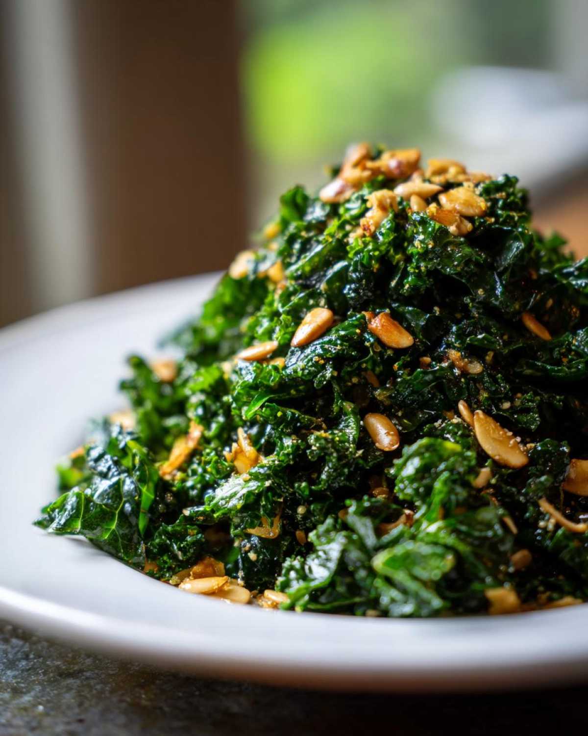 A close-up of a mound of massaged kale, resembling the Copycat Kale Crunch Salad, topped with toasted nuts or seeds.