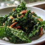A close-up of vibrant green kale leaves tossed in a creamy dressing, topped with crunchy pecans, resembling the Copycat Kale Crunch Salad.