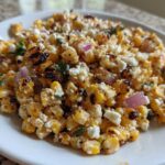 A close-up of grilled corn kernels mixed with white cheese crumbles and red onion, representing the Copycat Mexican Grill Corn Salsa.