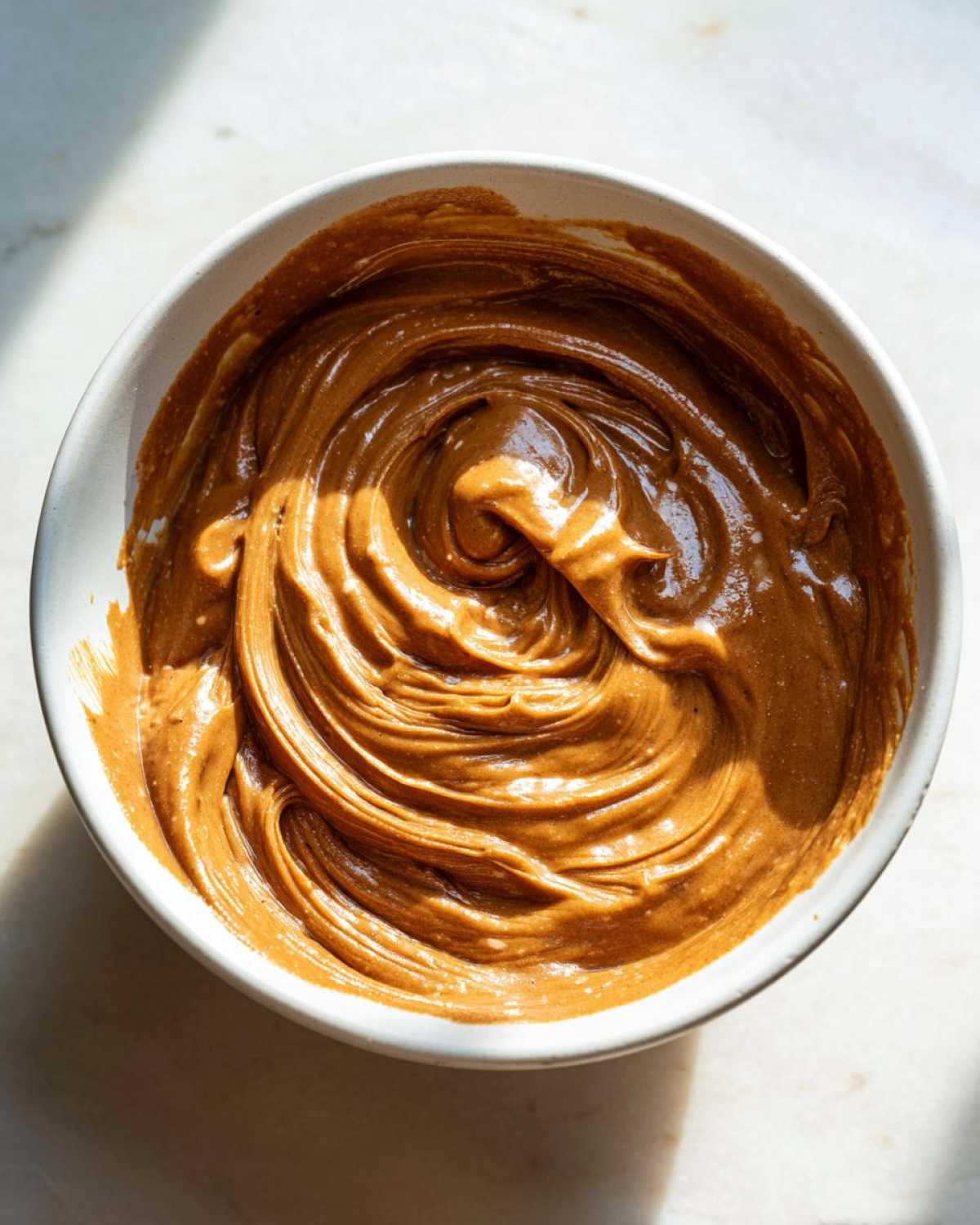 Top-down view of thick, creamy Easy 5-Minute Peanut Sauce for Noodles swirled in a white bowl.