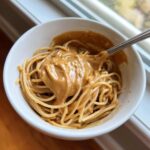 Close-up of noodles being mixed with a thick, creamy Easy 5-Minute Peanut Sauce in a white bowl.