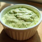 Close-up of creamy Easy 5-Minute Salsa Verde Yogurt Dip topped with fresh herbs in a white fluted bowl.