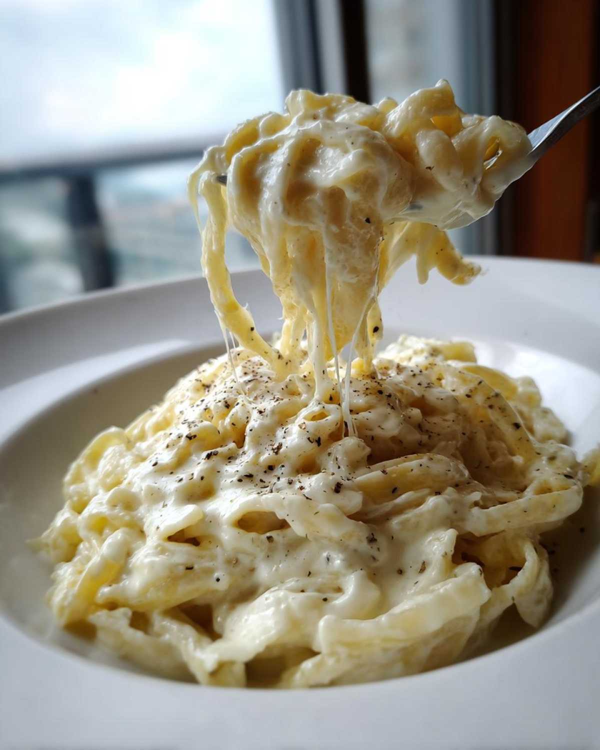A fork lifting fettuccine noodles coated in creamy Easy Cottage Cheese Alfredo Sauce, showing a cheese pull.