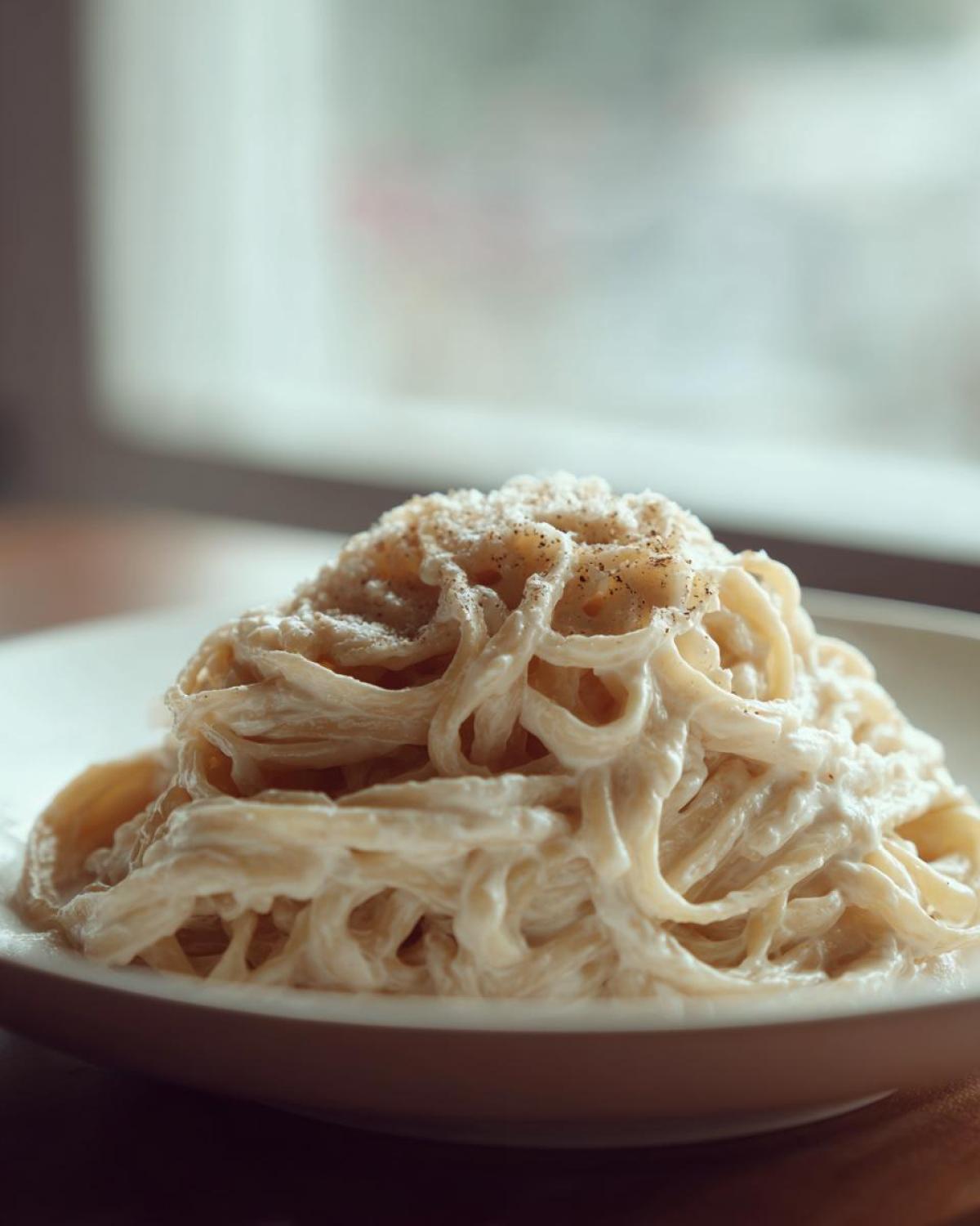 A close-up of fettuccine pasta generously coated in a creamy Easy Cottage Cheese Alfredo Sauce and topped with black pepper.