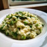 A close-up, appetizing shot of Easy Creamy Asparagus Risotto topped with fresh herbs and whole asparagus spears.