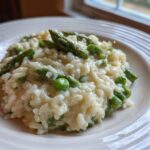 A close-up of a serving of Easy Creamy Asparagus Risotto with bright green asparagus tips and peas on a white plate.