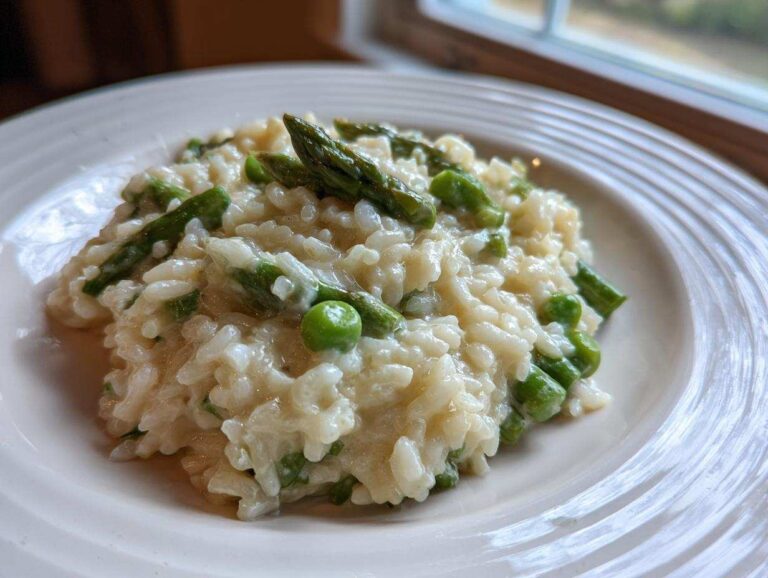 A close-up of a serving of Easy Creamy Asparagus Risotto with bright green asparagus tips and peas on a white plate.
