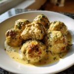 Six Easy Creamy Greek Chicken Meatballs covered in a rich, yellow sauce and garnished with fresh dill.