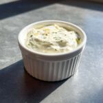 A small white ramekin filled with creamy Easy Greek Yogurt Caesar Dressing, topped with herbs and Parmesan.