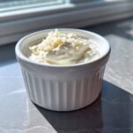 A white ramekin filled with thick Easy Greek Yogurt Caesar Dressing, topped with grated cheese.