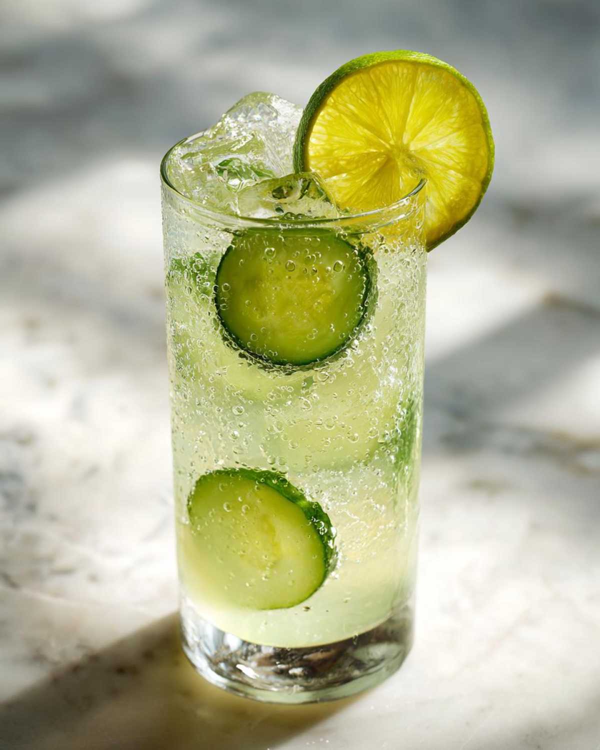 A tall glass filled with Easy Iced Cucumber Lime Agua Fresca, ice, cucumber slices, and a lime wheel garnish.