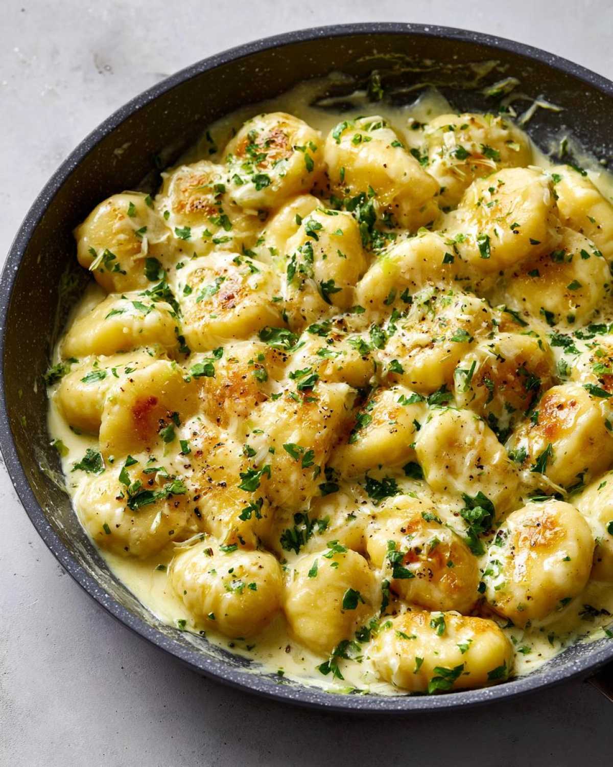 Close-up of Easy One-Pan Creamy Garlic Butter Gnocchi simmering in a dark skillet, topped with parsley.