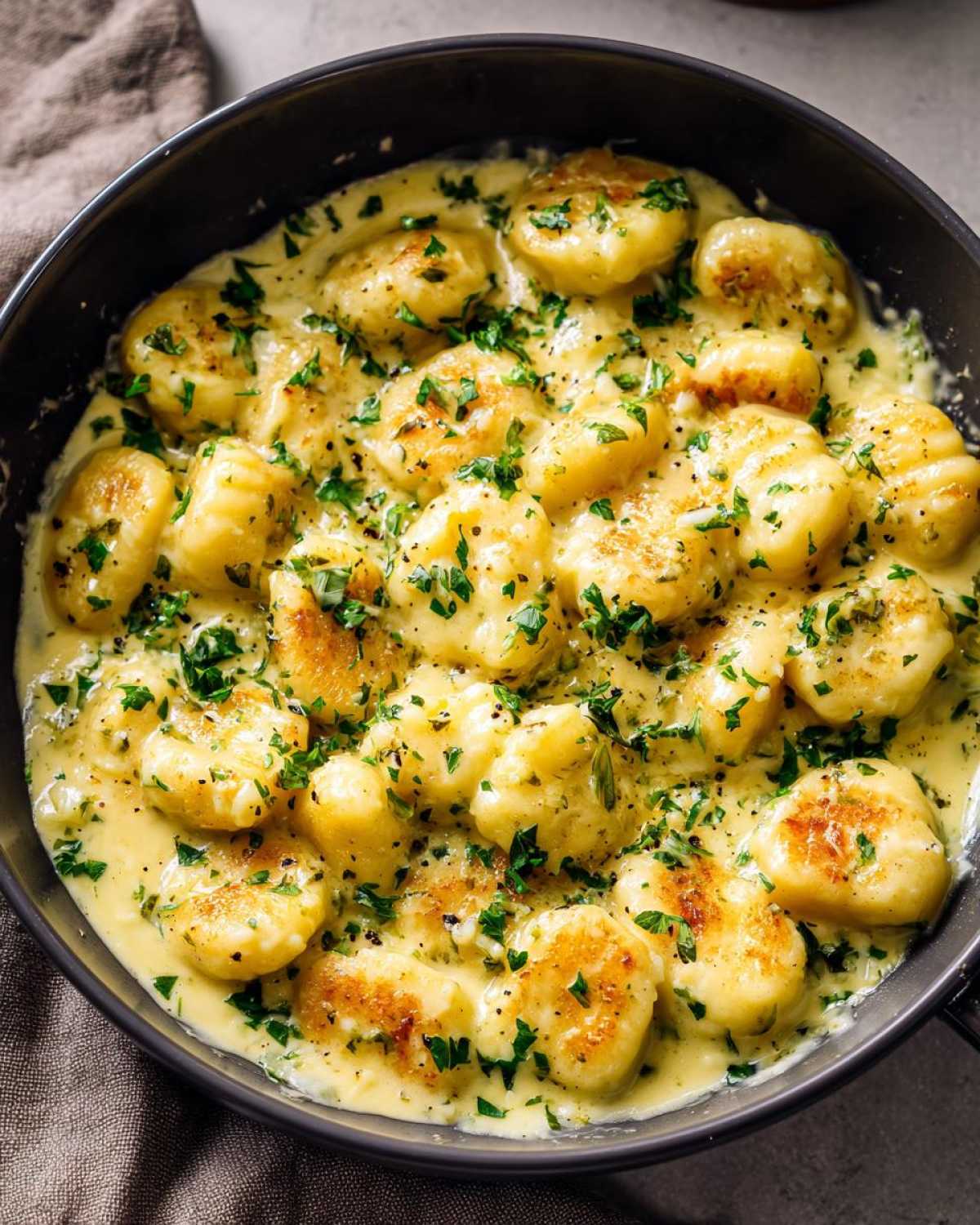Close-up of golden pan-seared gnocchi swimming in a rich, creamy garlic butter sauce, topped with fresh parsley.