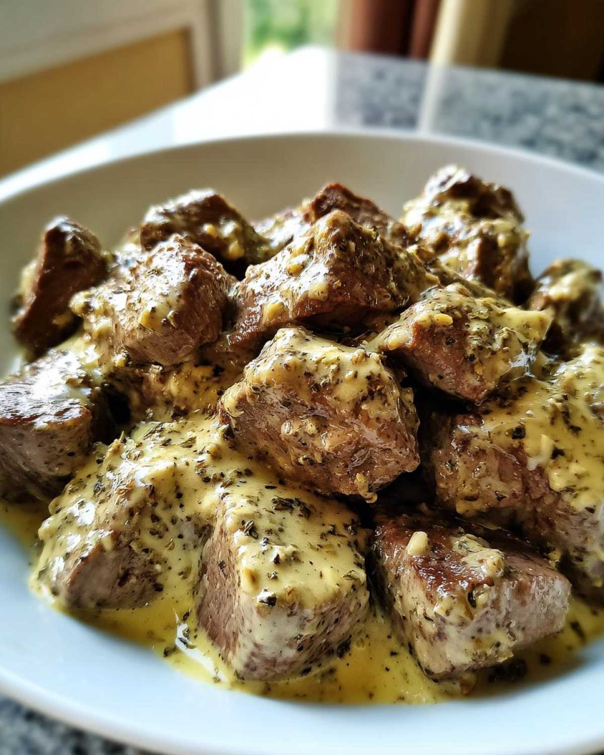 Close-up of tender steak bites smothered in a rich, creamy garlic sauce with visible herbs.