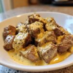 Close-up of tender steak bites smothered in a rich, creamy garlic sauce, ready to eat.