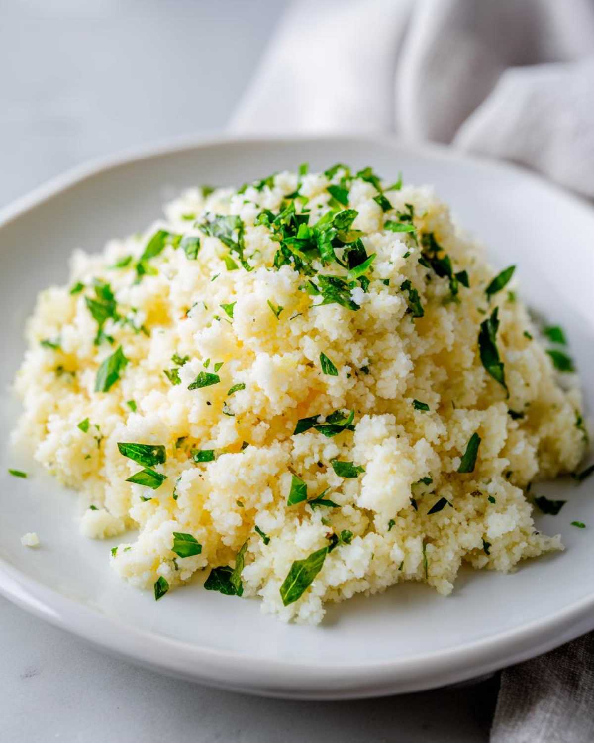 A mound of fluffy Easy One-Pot Creamy Lemon Herb Couscous topped generously with fresh chopped parsley.