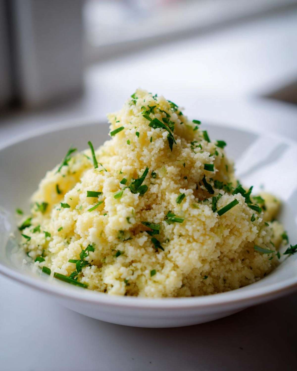 A mound of fluffy Easy One-Pot Creamy Lemon Herb Couscous topped generously with fresh chopped green herbs.