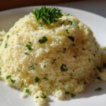 A mound of light yellow Easy One-Pot Creamy Lemon Herb Couscous garnished with fresh chopped parsley.