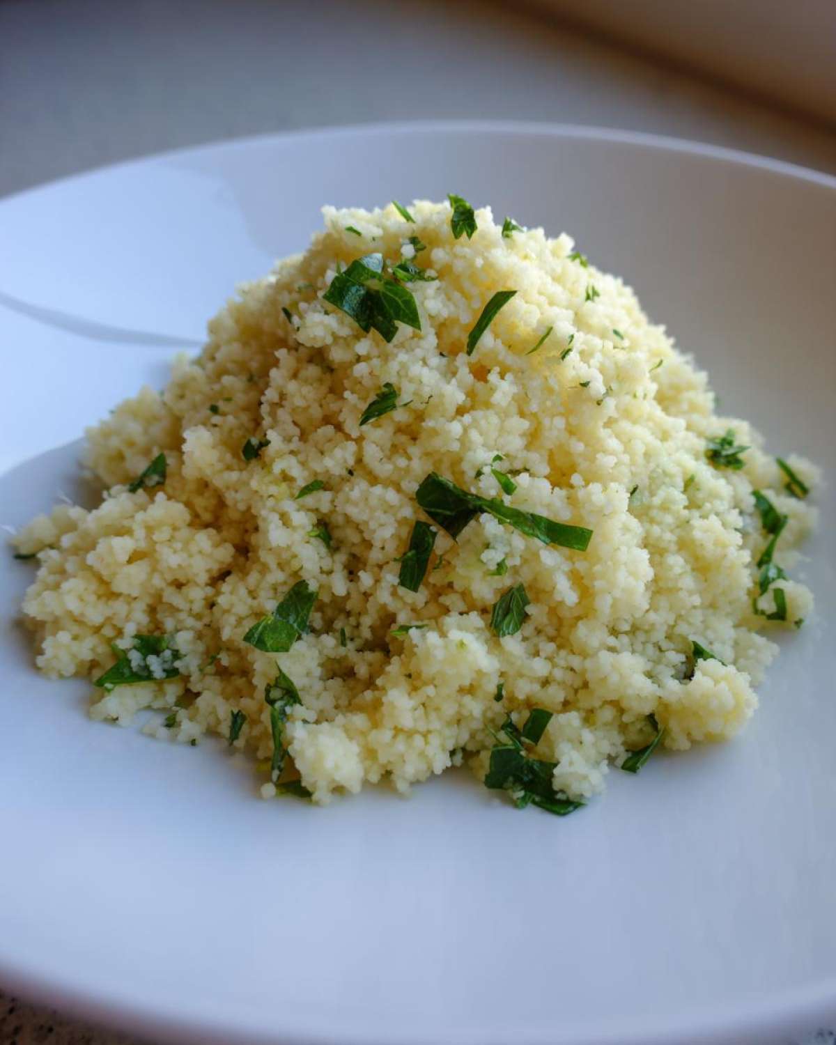 A mound of fluffy Easy One-Pot Creamy Lemon Herb Couscous garnished with chopped fresh parsley on a white plate.