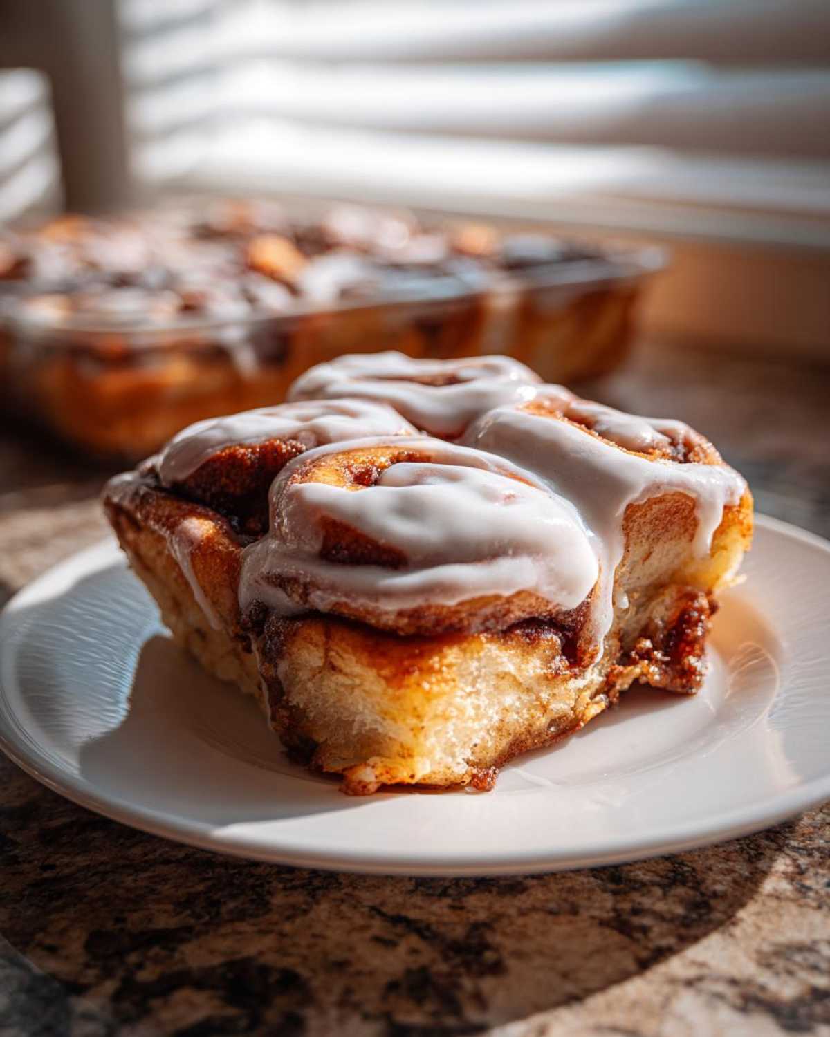 Close-up of a serving of Easy Sheet Pan Cinnamon Roll Pancake Bake, drizzled with white icing, on a white plate.