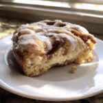 A close-up of a single, fluffy portion of the Easy Sheet Pan Cinnamon Roll Pancake Bake, topped with white icing.