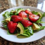 Close-up of an Easy Strawberry Avocado Salad featuring sliced strawberries, avocado chunks, and mixed greens on a white plate.