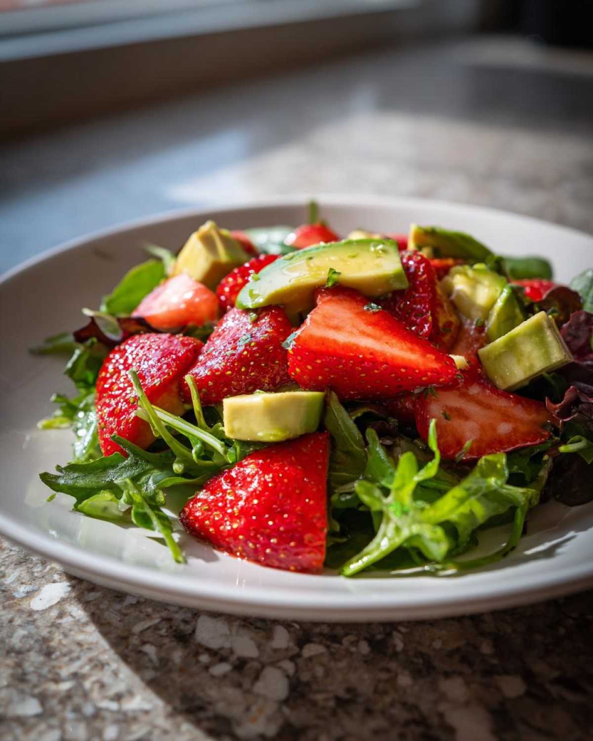 A vibrant bowl featuring an Easy Strawberry Avocado Salad with bright red strawberries and green avocado chunks over mixed greens.